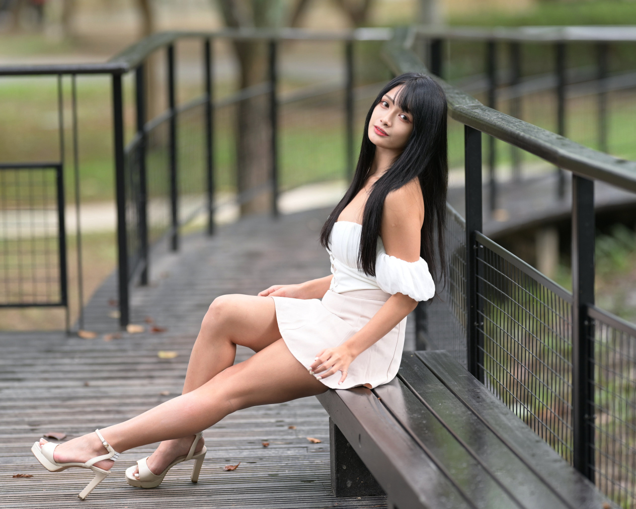 Красивая длинноволосая азиатка в белом платье сидит на лавке