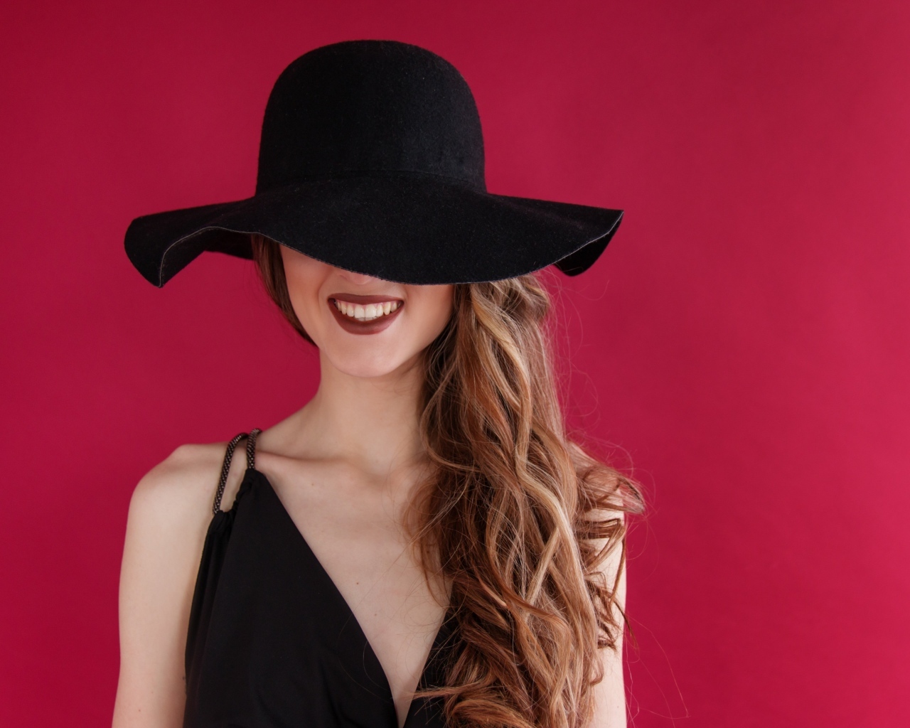 Черная шляпа на лице у девушки на розовом фоне