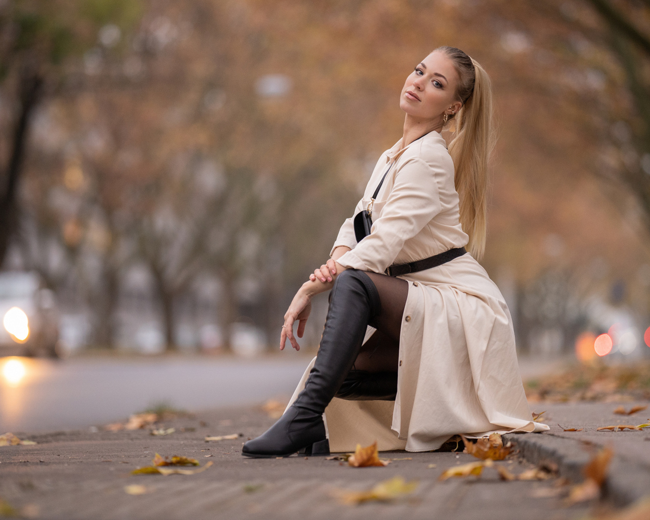 Девушка блондинка сидит в пальто в парке
