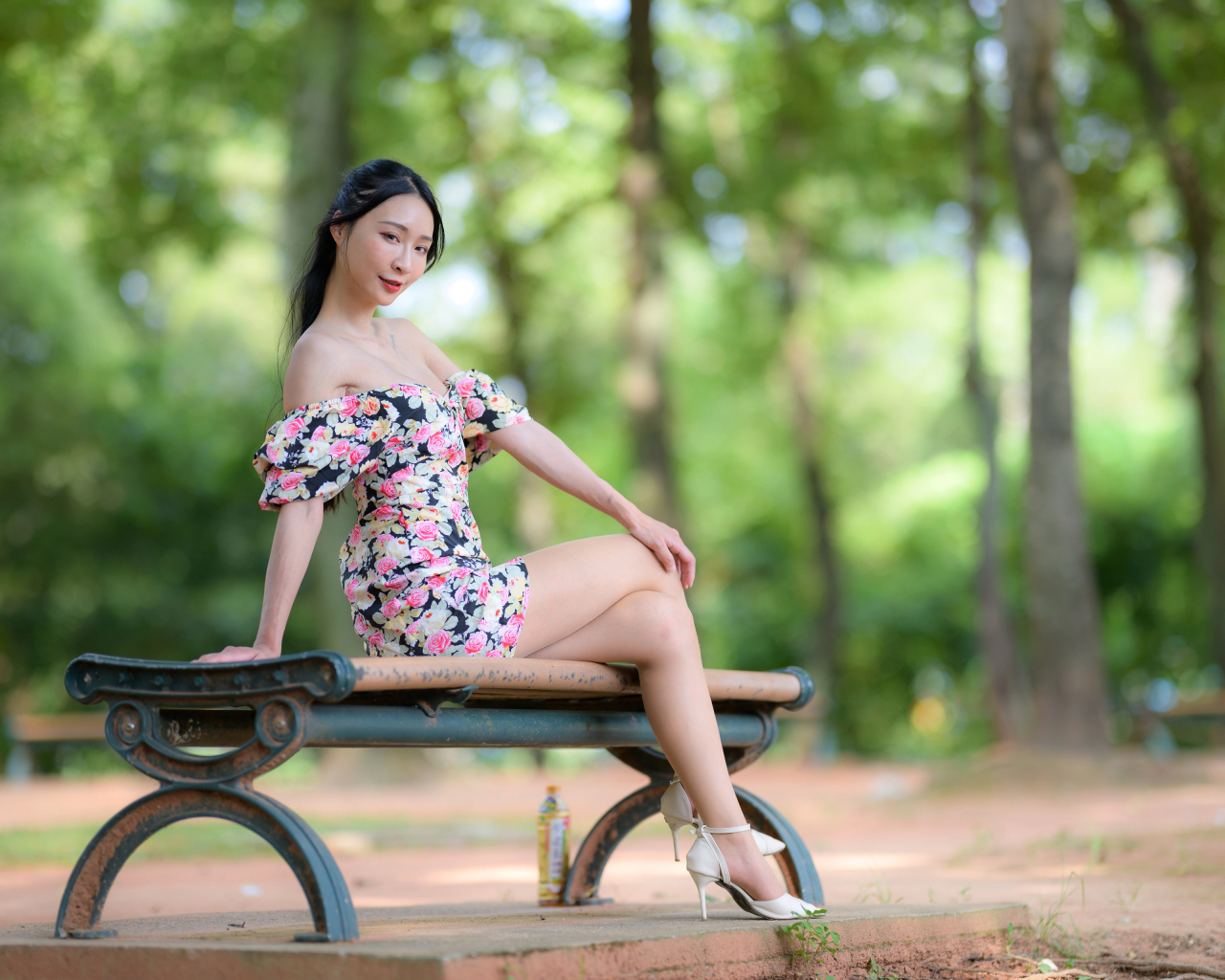 Милая девушка азиатка в платье сидит на лавке в парке