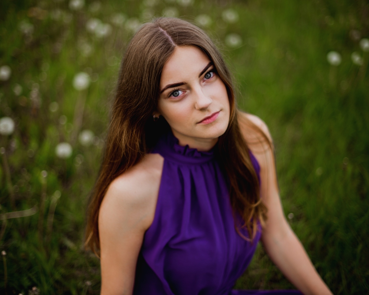 Милая девушка в фиолетовом платье сидит на траве
