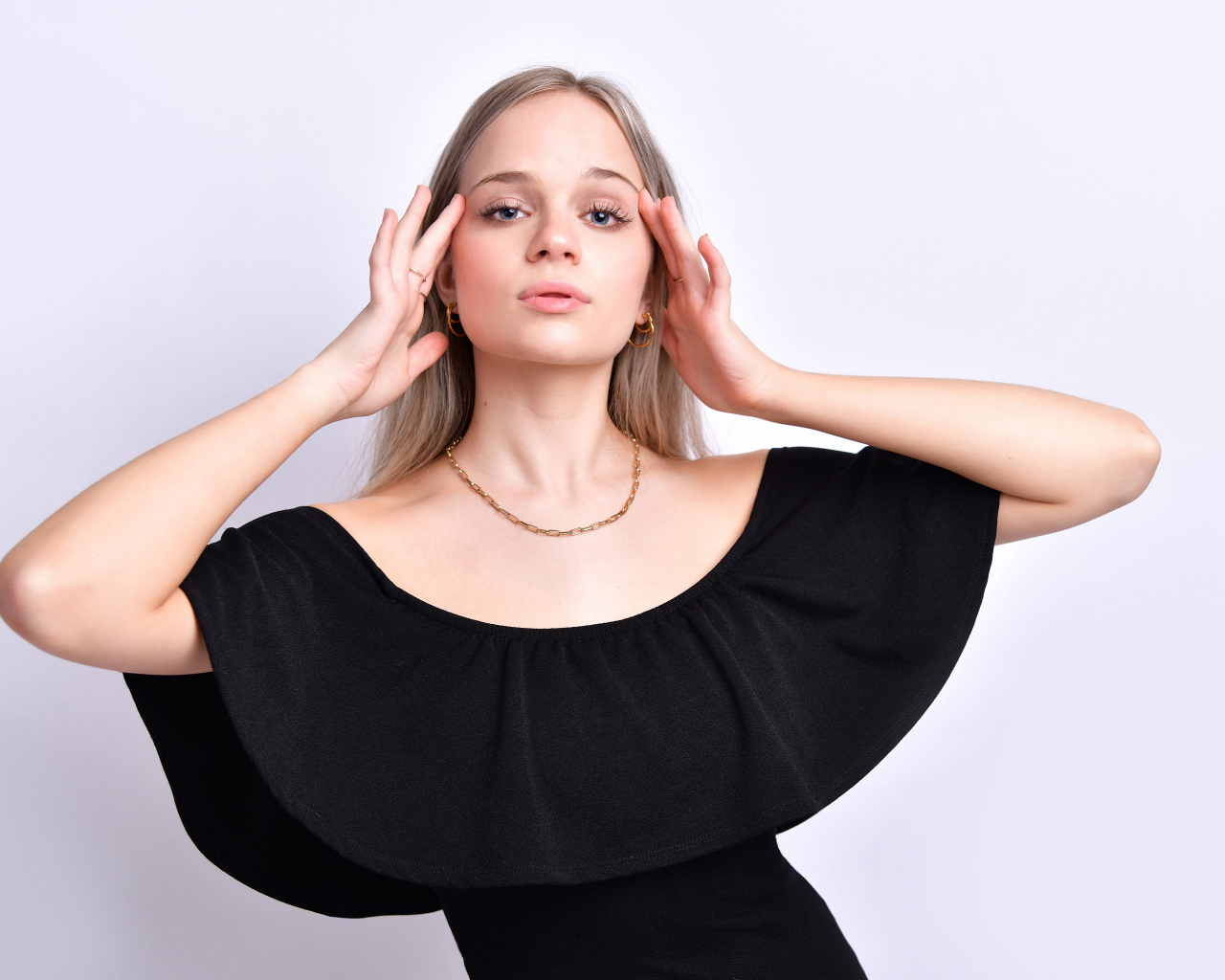 Девушка в черном платье с руками у головы на белом фоне