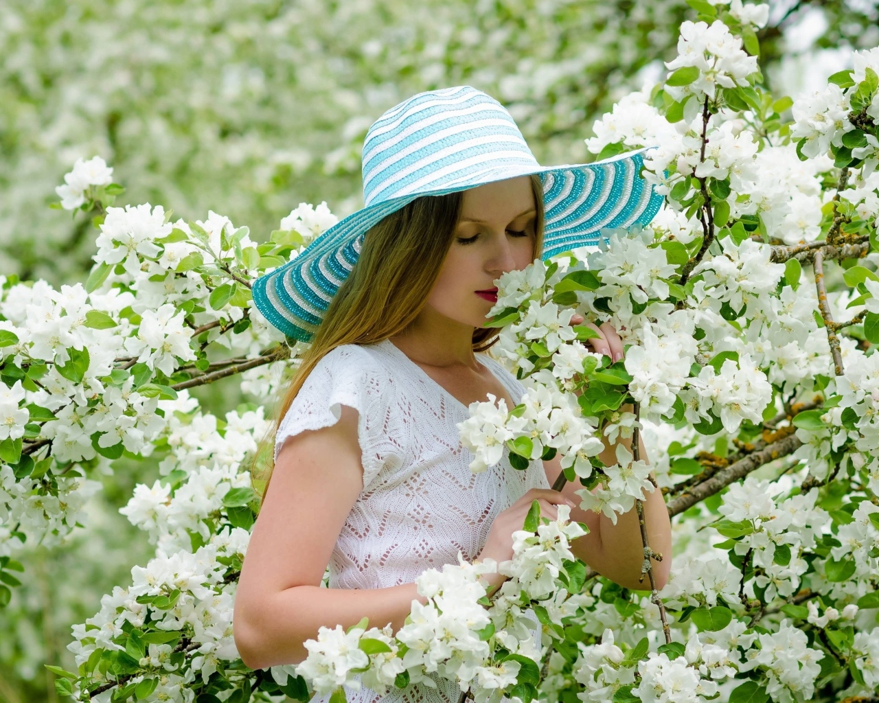 Девушка в шляпе нюхает ветку яблони 