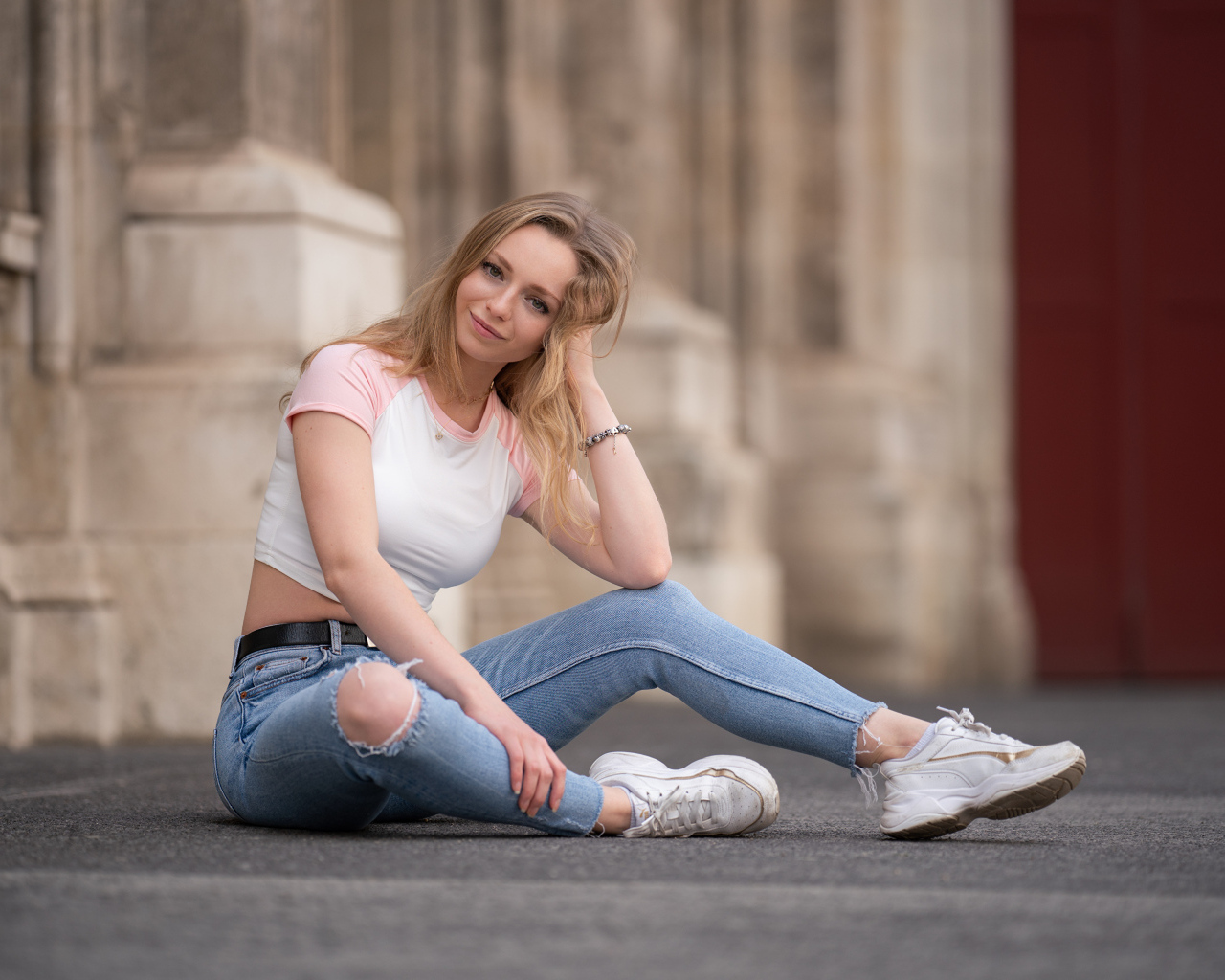 Девушка в рваных джинсах сидит на асфальте
