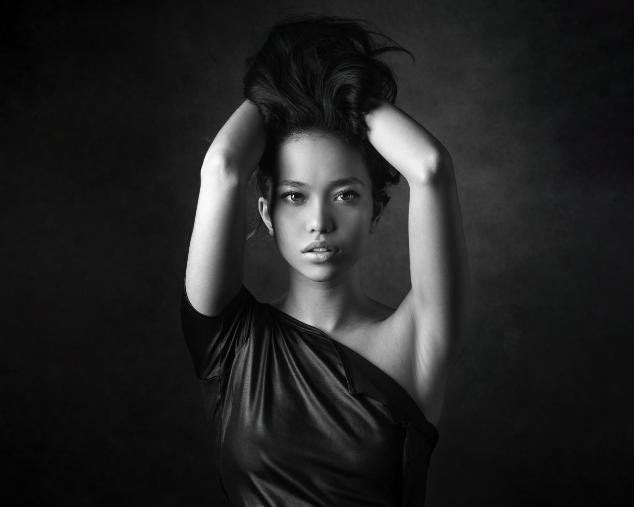 Девушка модель с руками в волосах  у стены