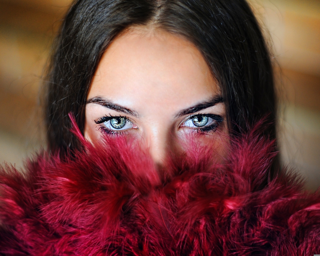 Девушка с красивыми глазами закрыла лицо красными перьями