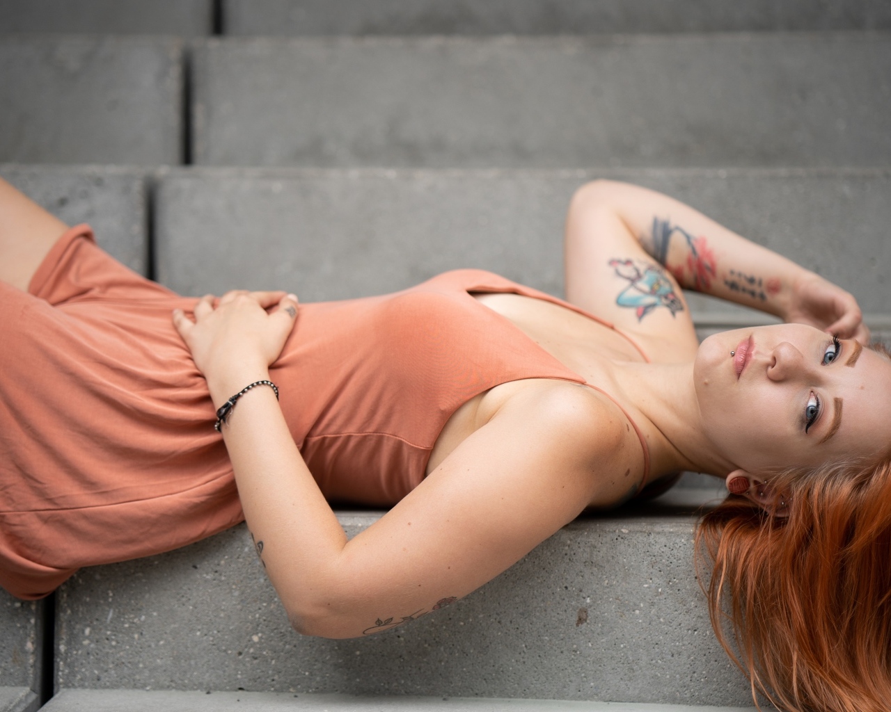 Рыжеволосая девушка с татуировками лижет на ступеньках