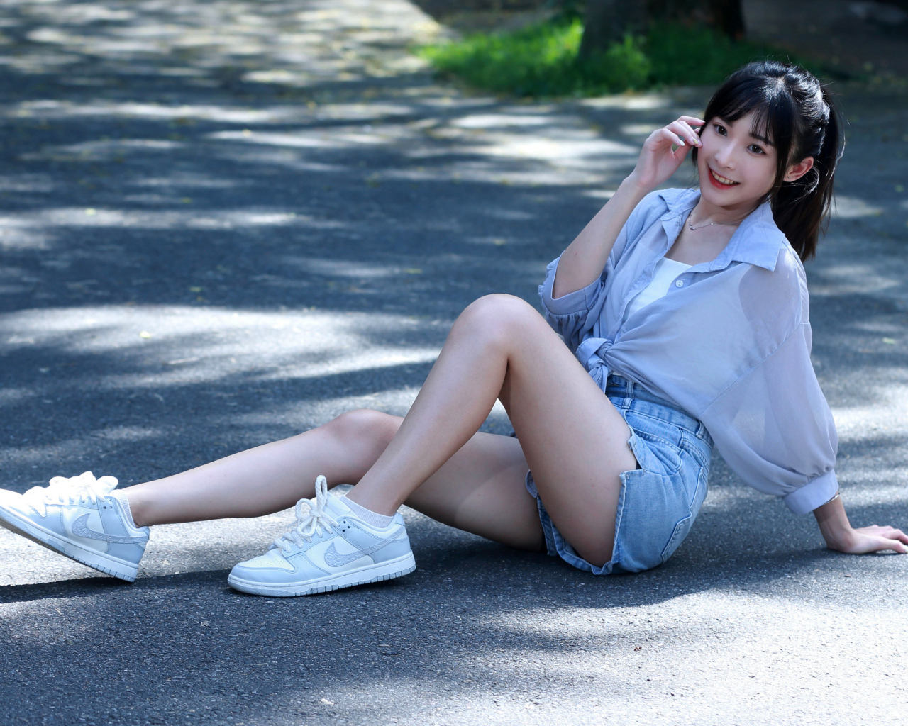 Улыбающаяся девушка азиатка в кедах сидит на дороге