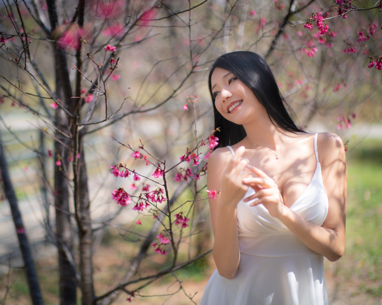 Улыбающаяся девушка в белом платье у дерева с цветами