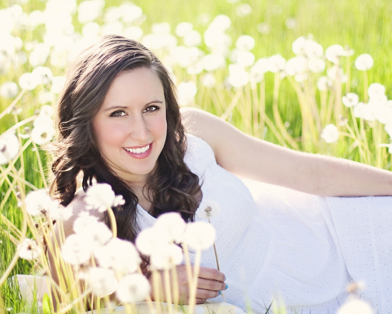 Улыбающаяся девушка лежит на поле с одуванчиками
