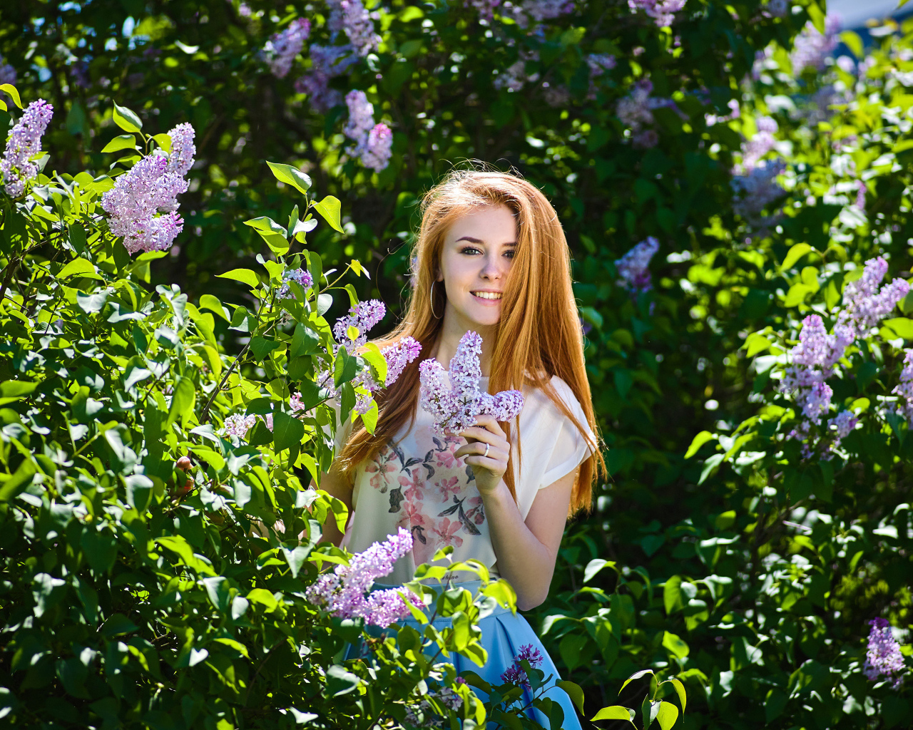 Улыбающаяся девушка стоит у куста сирени