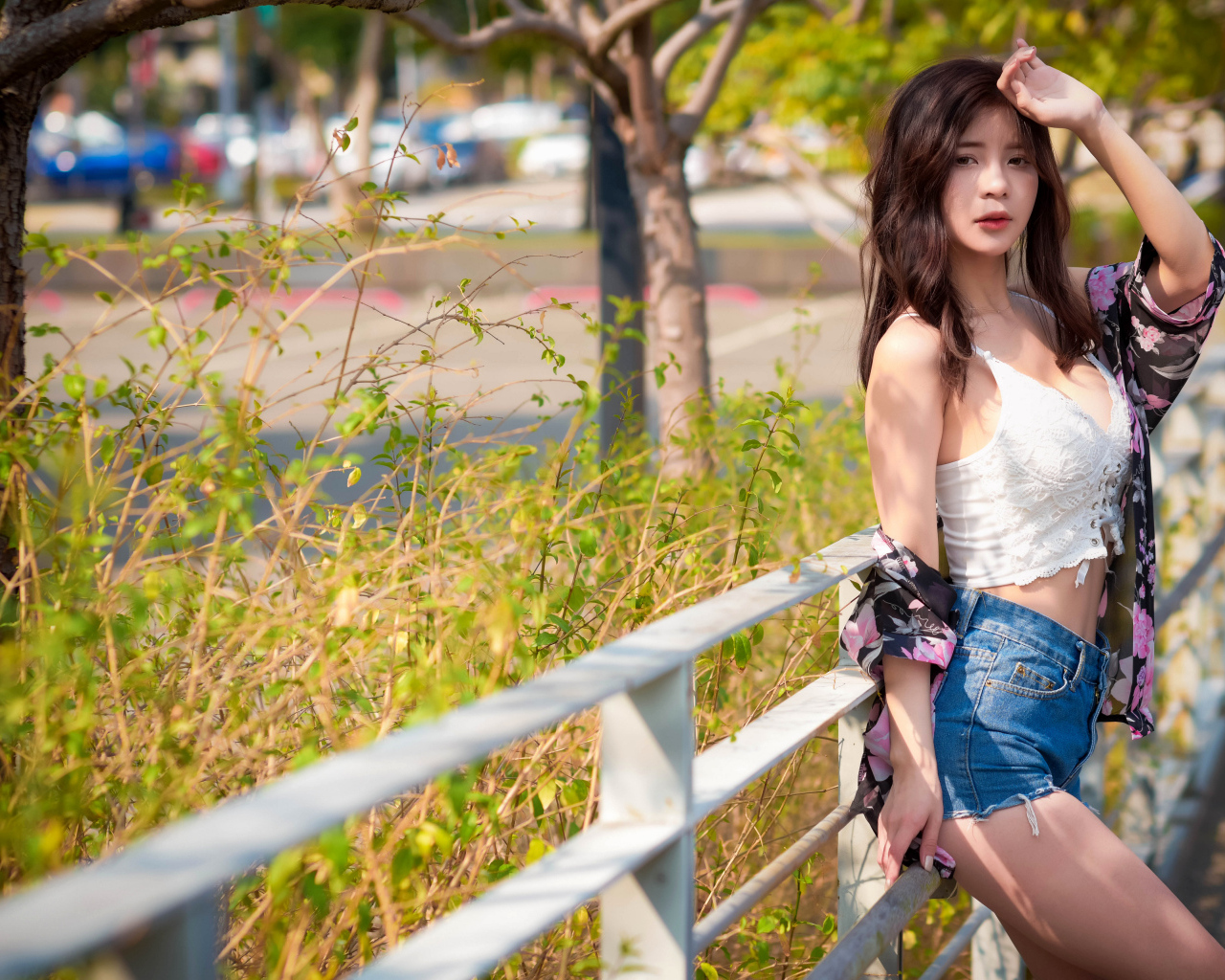 Молодая азиатка в синих шортах стоит у забора