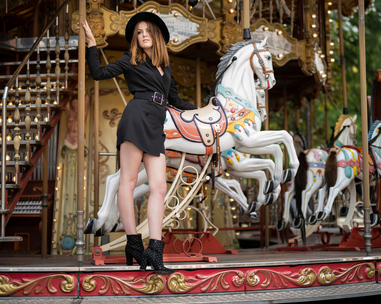 Молодая девушка в черном платье у карусели в парке