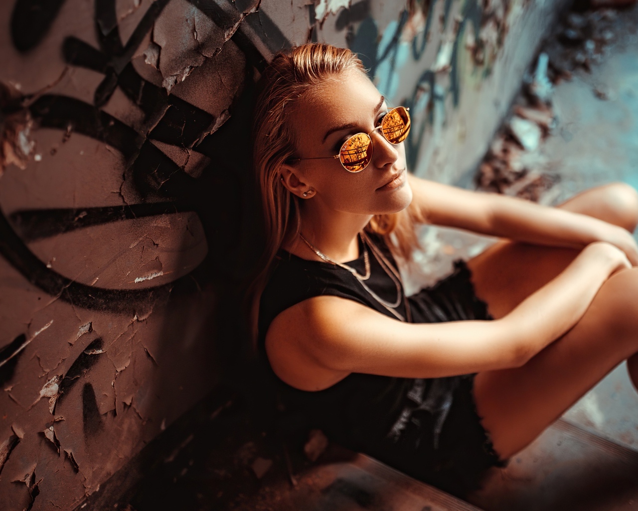 Молодая девушка в очках сидит у стены