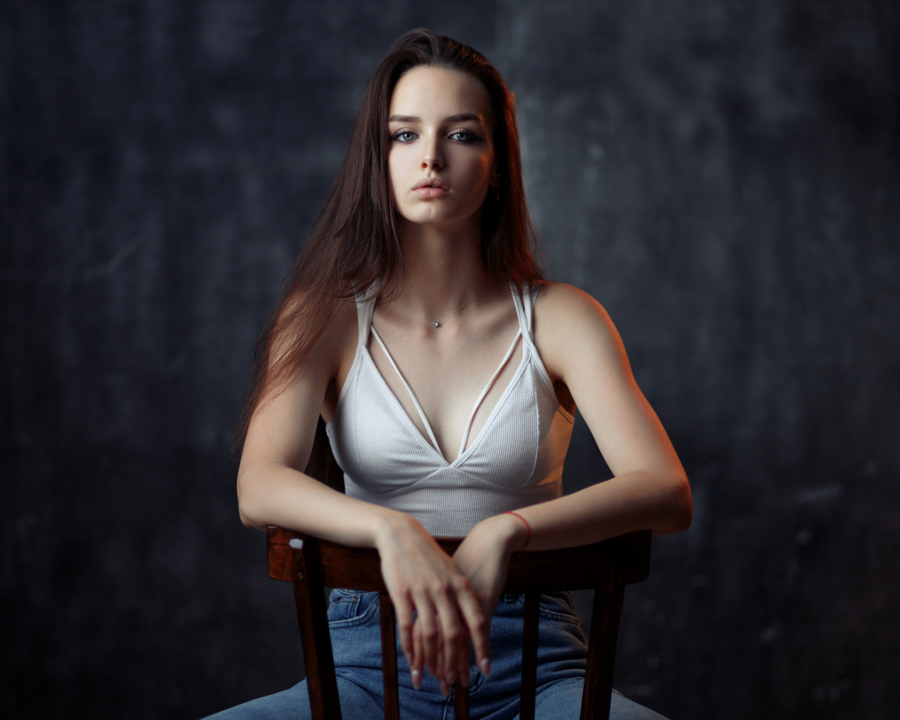 Молодая длинноволосая девушка сидит на деревянном стуле
