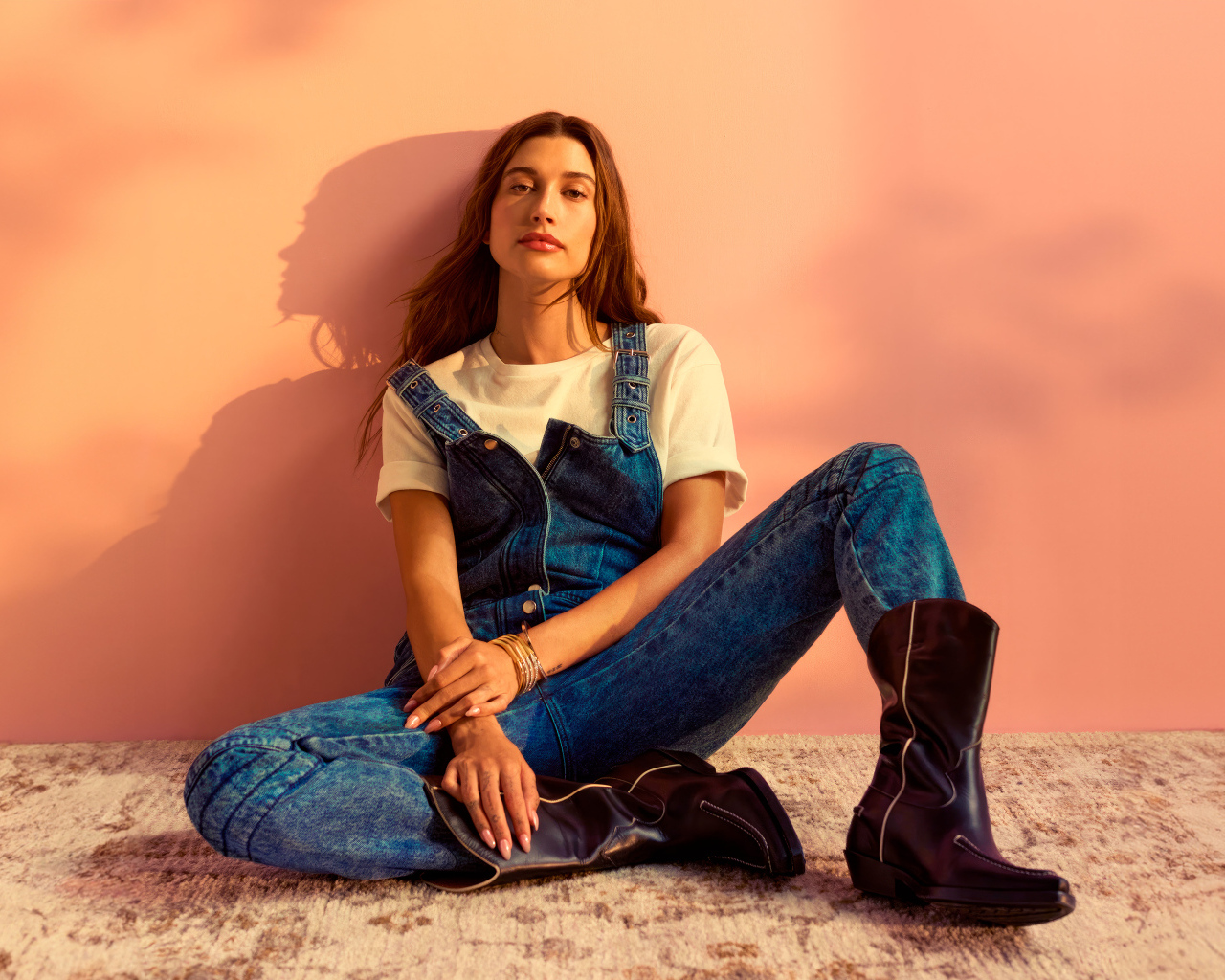 Американская модель Хейли Болдуин в джинсовом комбинезоне сидит у стены