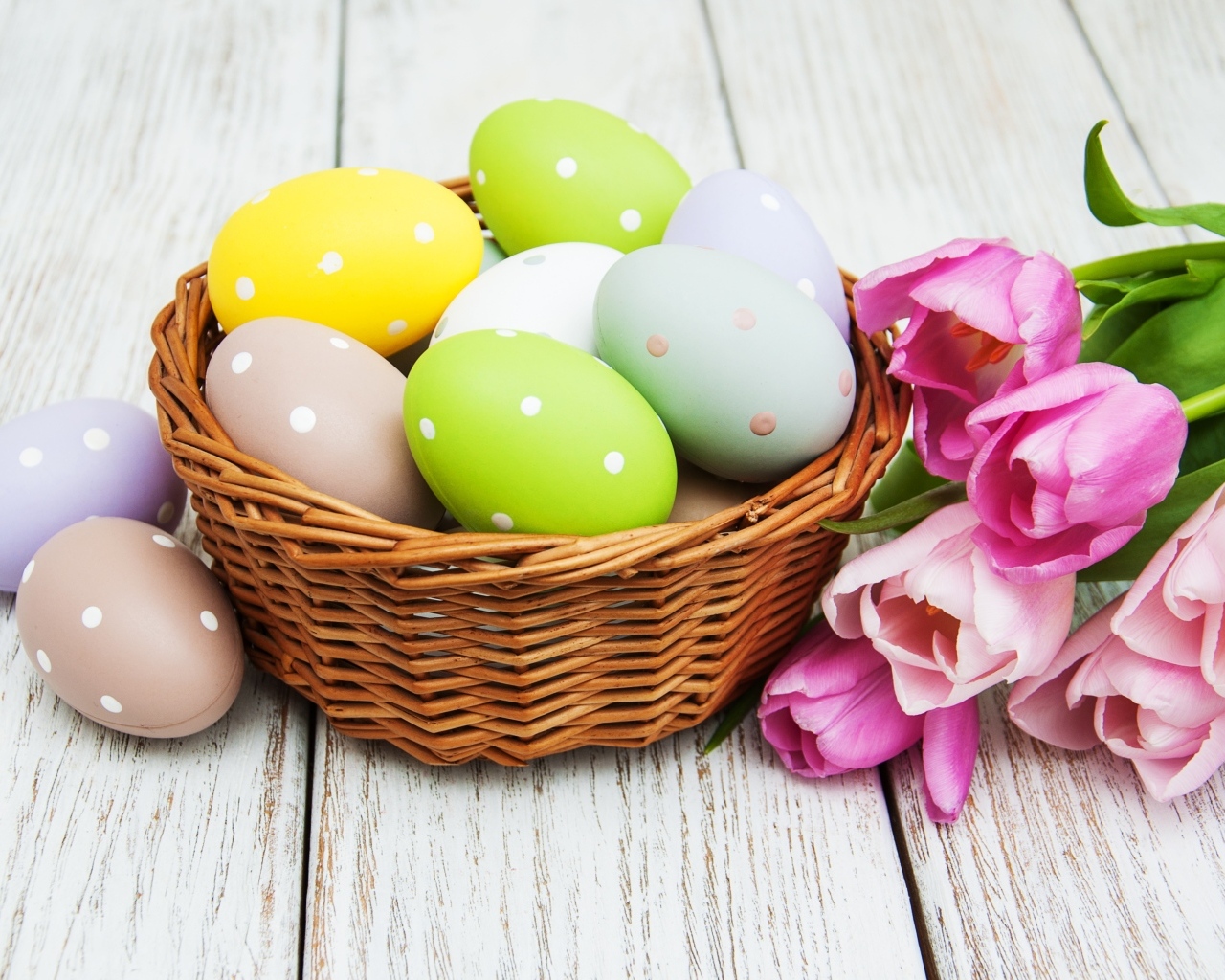 Корзина разноцветных яиц с тюльпанами на столе на Пасху