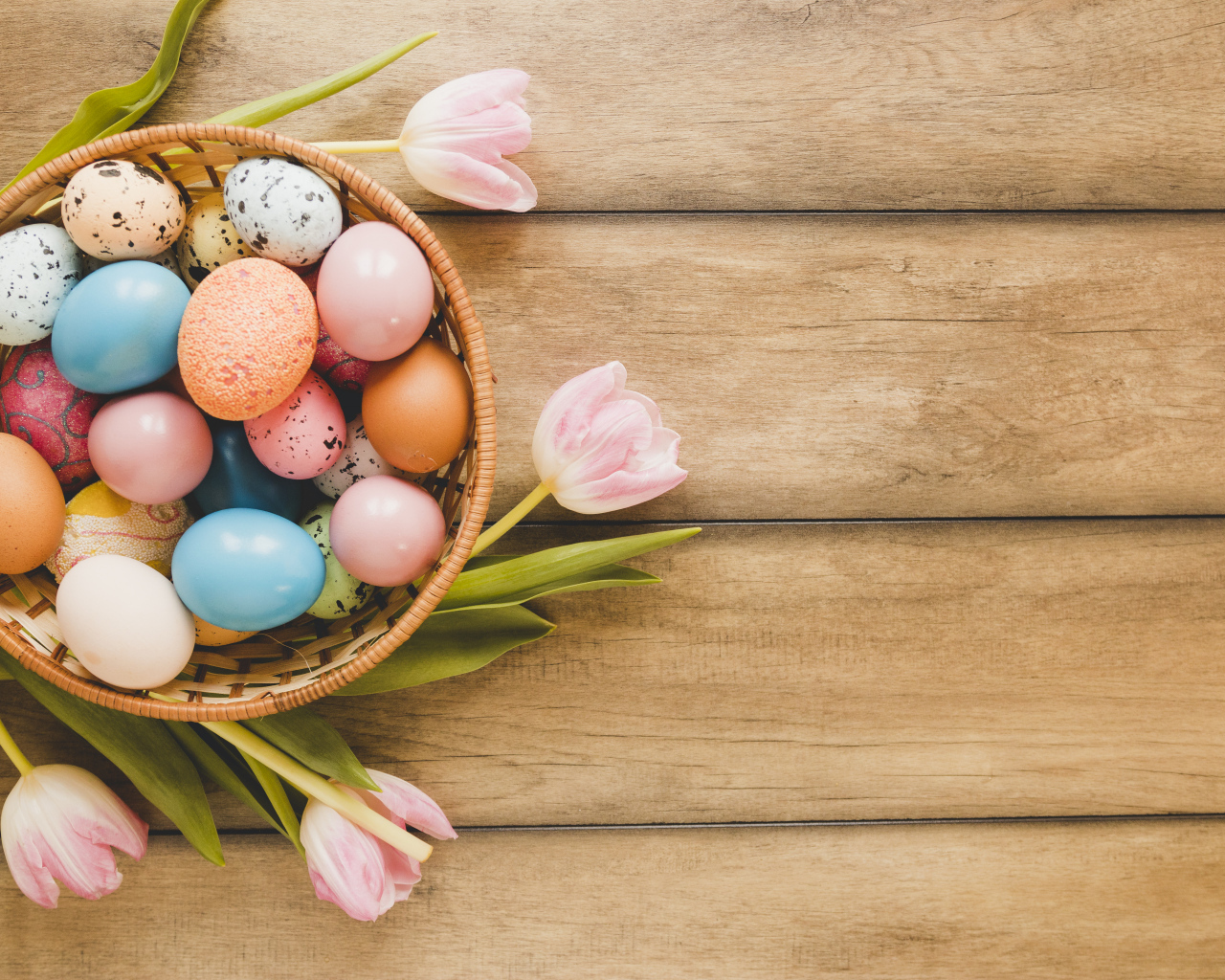 Корзина с крашеными яйцами и розовые тюльпаны на деревянном столе на Пасху