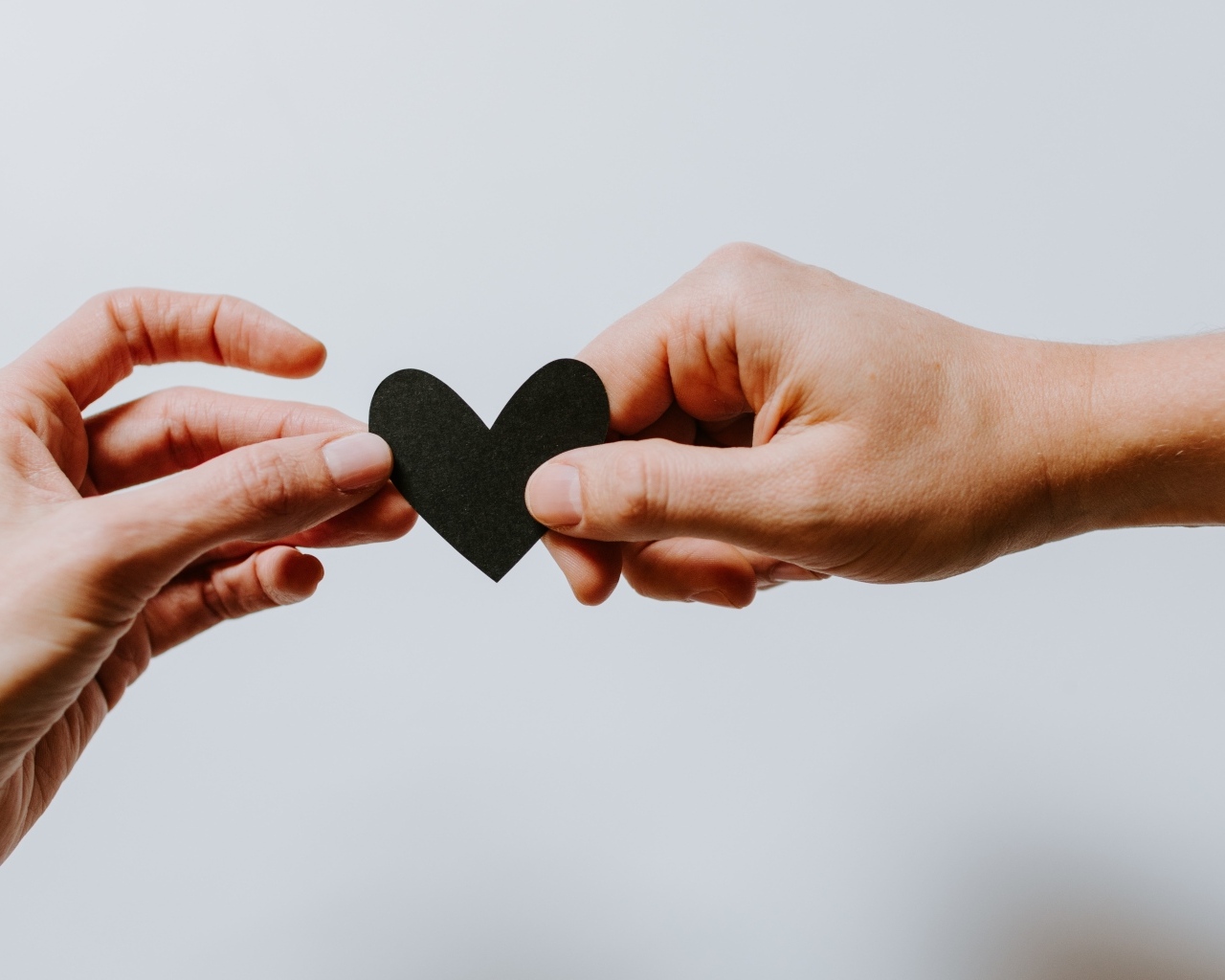 Черное бумажное сердце в руках на сером фоне