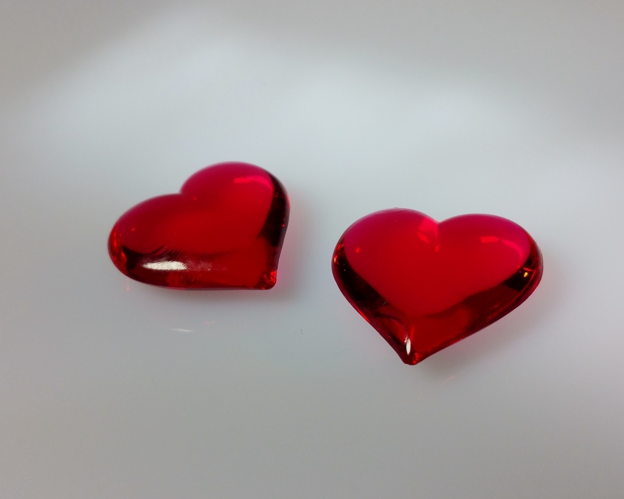 Два красных стеклянных сердца на сером фоне