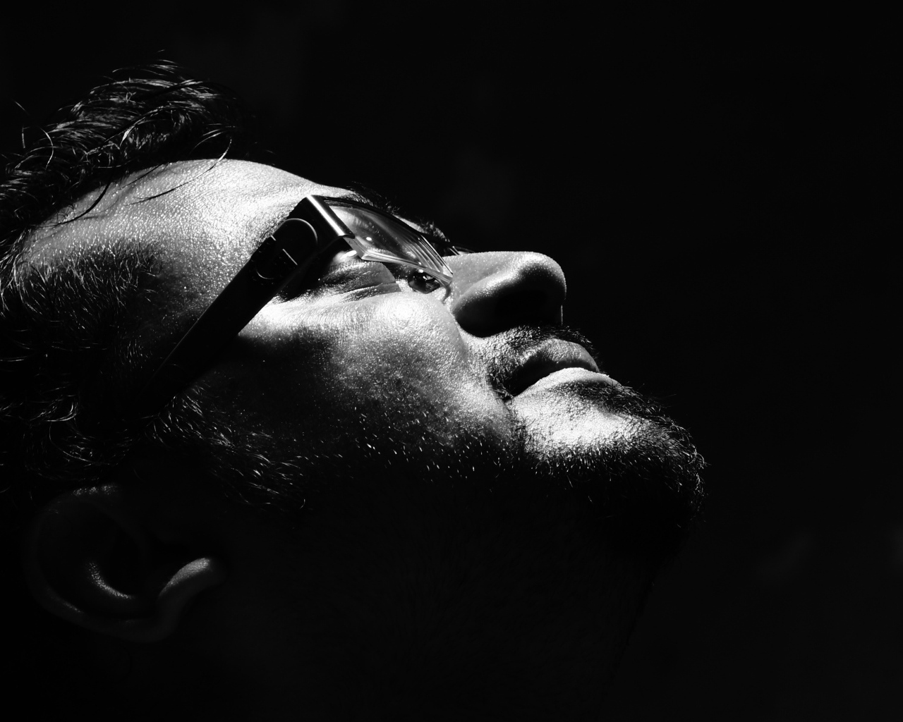 Мужчина в очках смотрит вверх на черном фоне