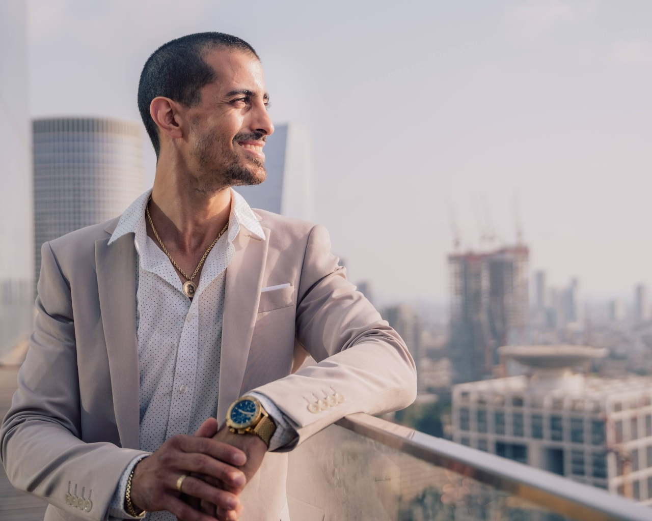 Улыбающийся стильный мужчина в костюме стоит на балконе 