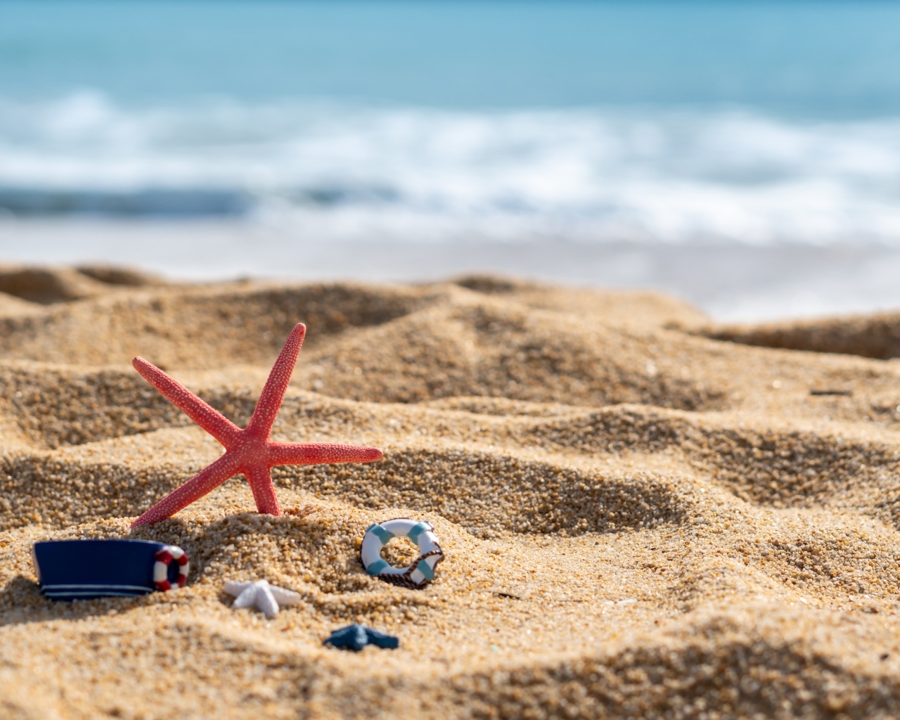 Красная морская звезда и игрушки на песке у моря летом