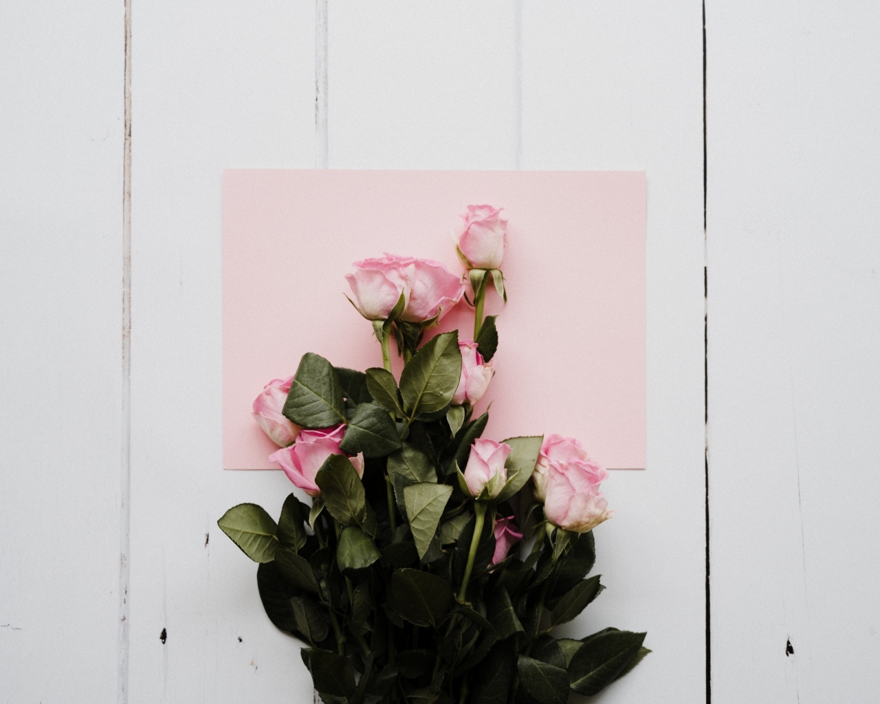 Букет роз с розовым листом бумаги на столе