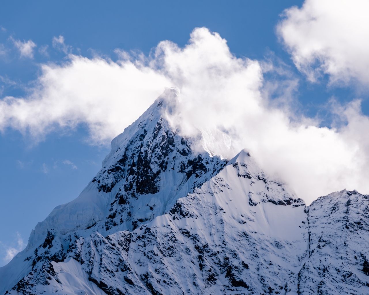 Острая заснеженная вершина горы в белых облаках