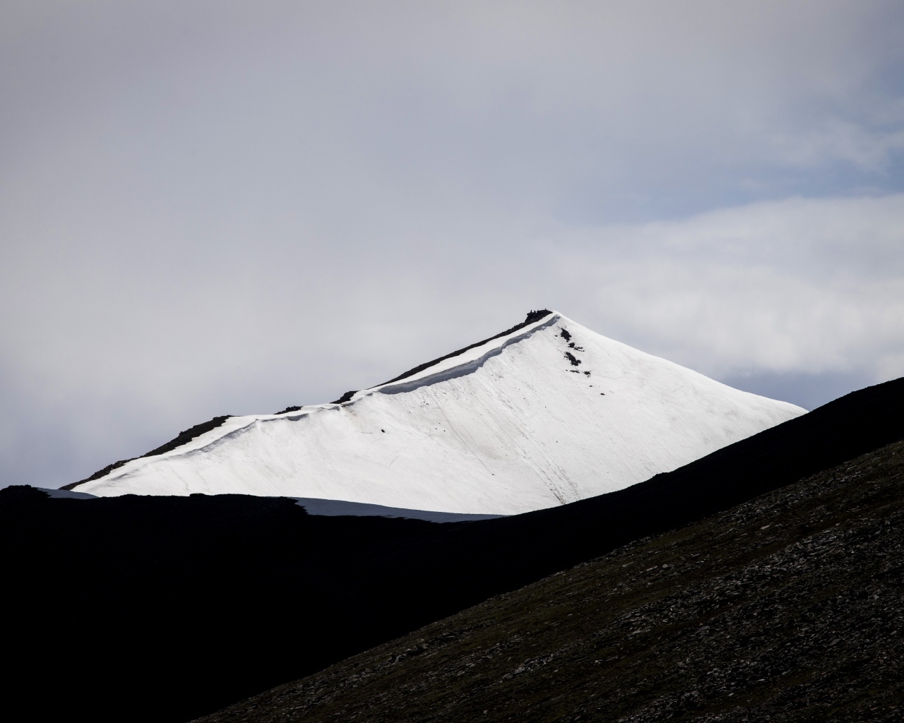 Заснеженная вершина горы под грозовым небом