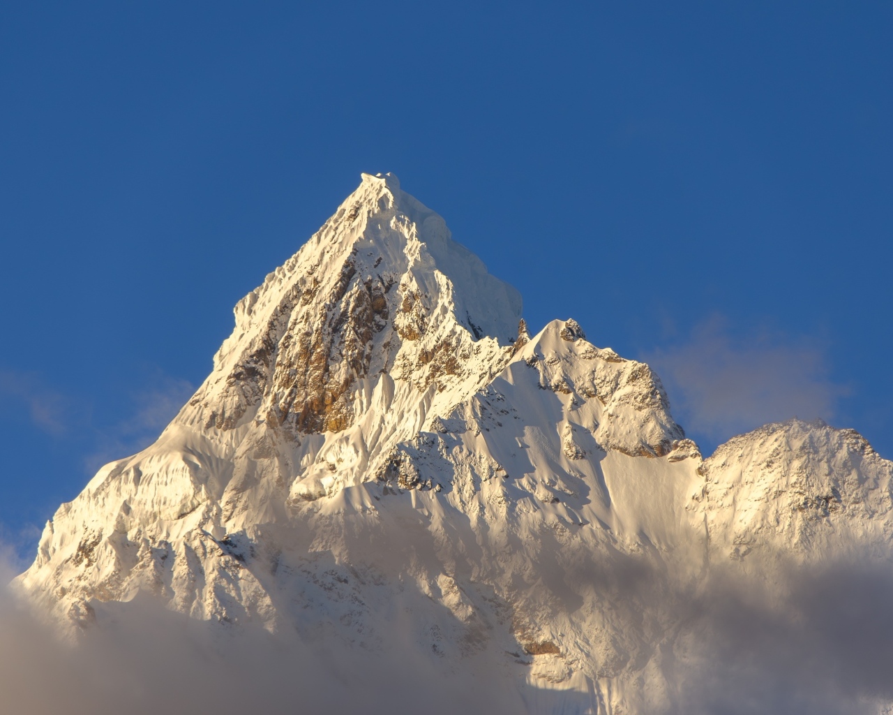 Крутая заснеженная вершина горы на голубом фоне