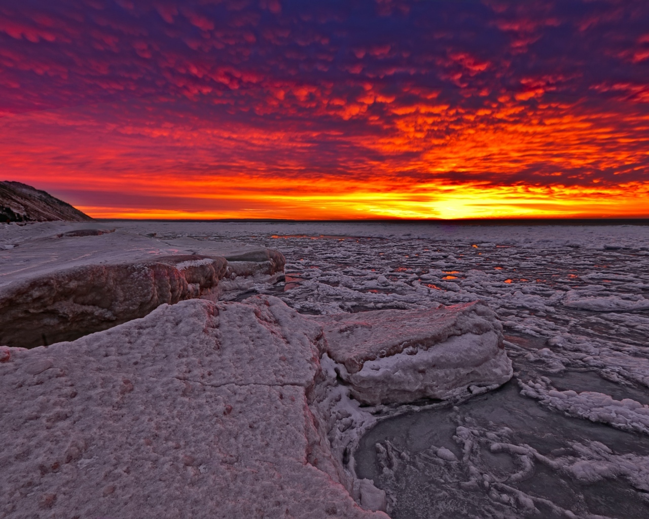 Красный закат солнца покрывает заледеневшее озеро 