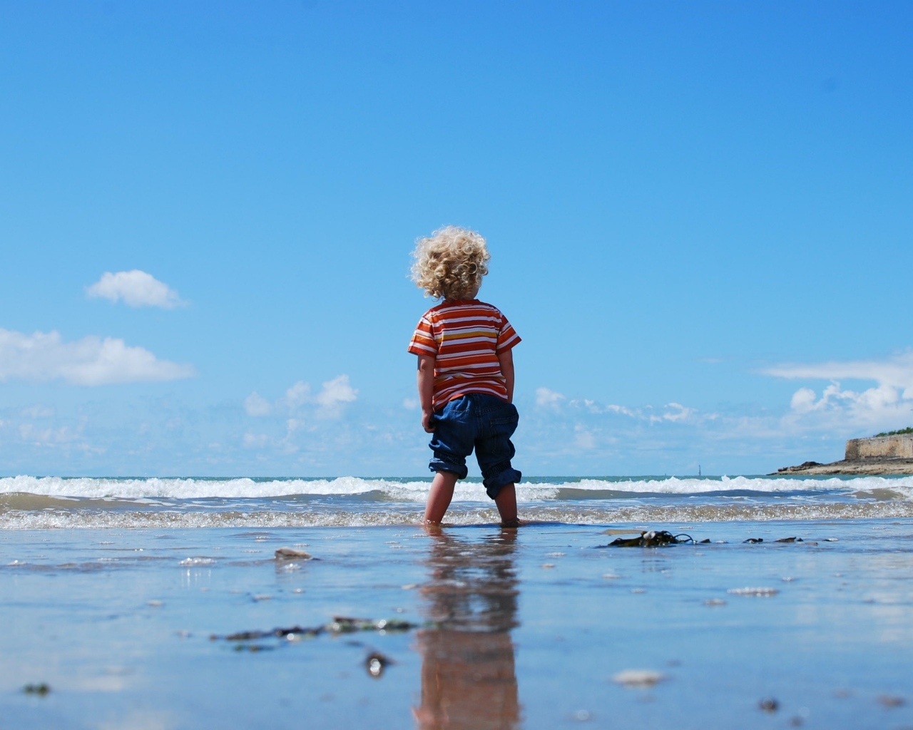 Маленький мальчик гуляет по мокрому песку у моря