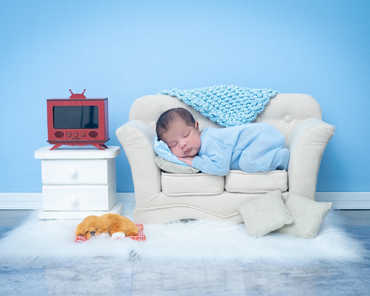 Новорожденный ребенок спит на белом диване на фоне голубой стены