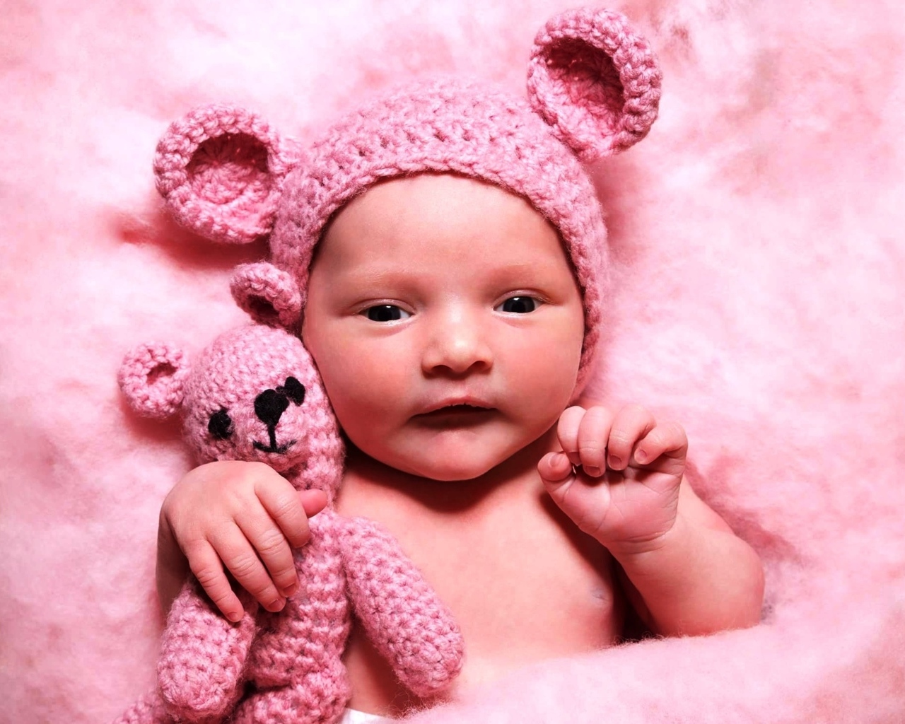 Грудной ребенок в розовой шапке с игрушкой в руке