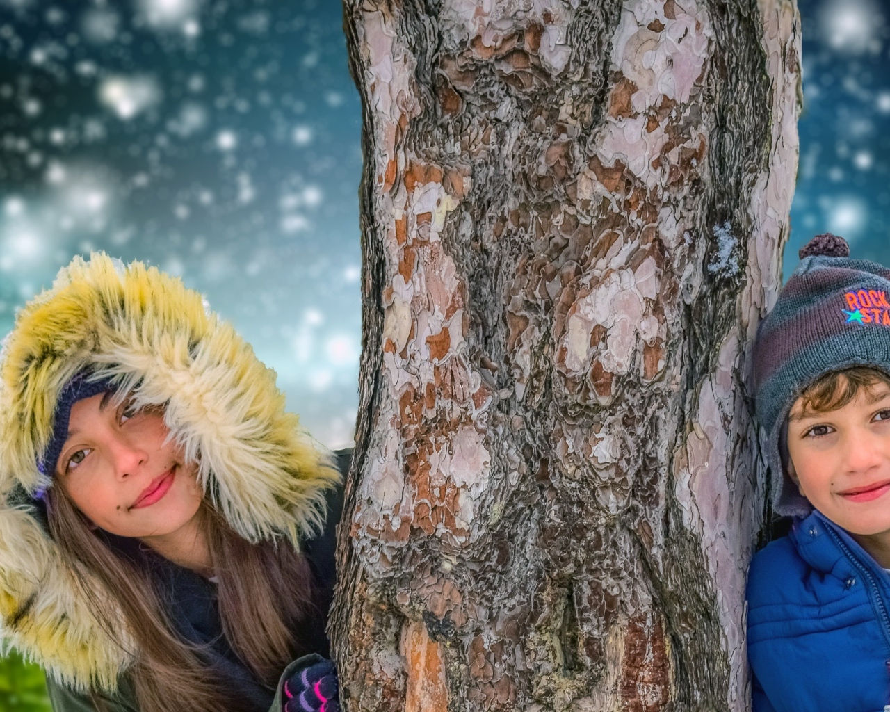 Мальчик и девочка стоят у дерева зимой