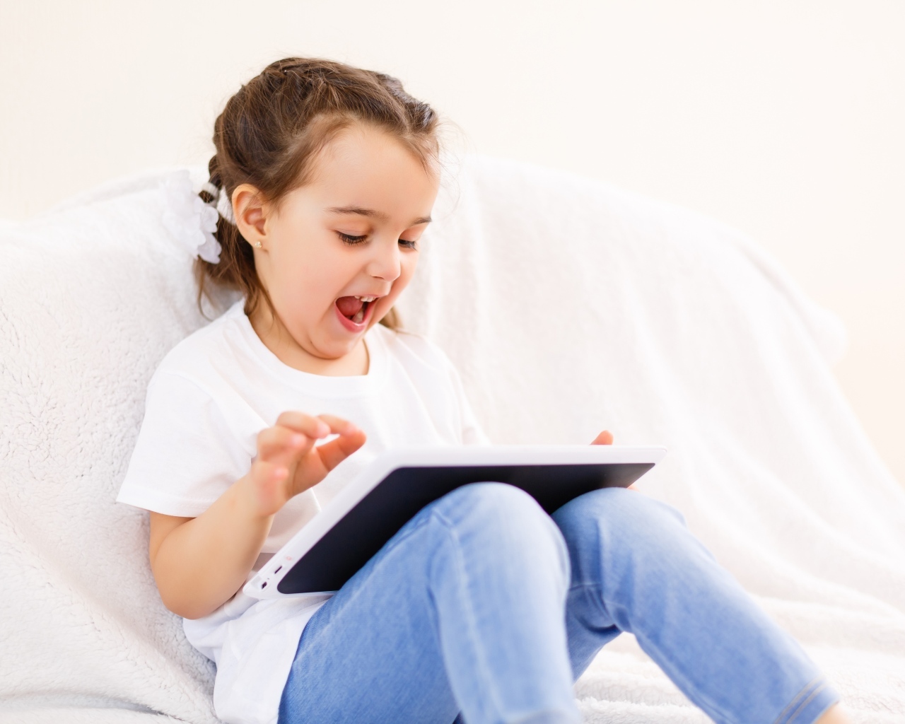 Веселая девочка с планшетом на кровати 