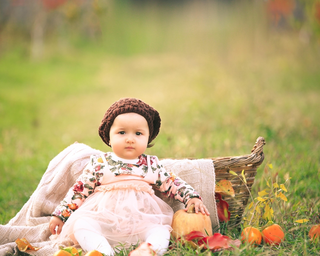 Милая маленькая девочка в шапке сидит на траве 