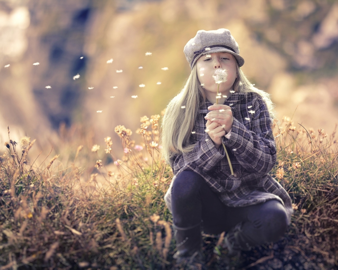 Девочка в кепке сдувает одуванчик