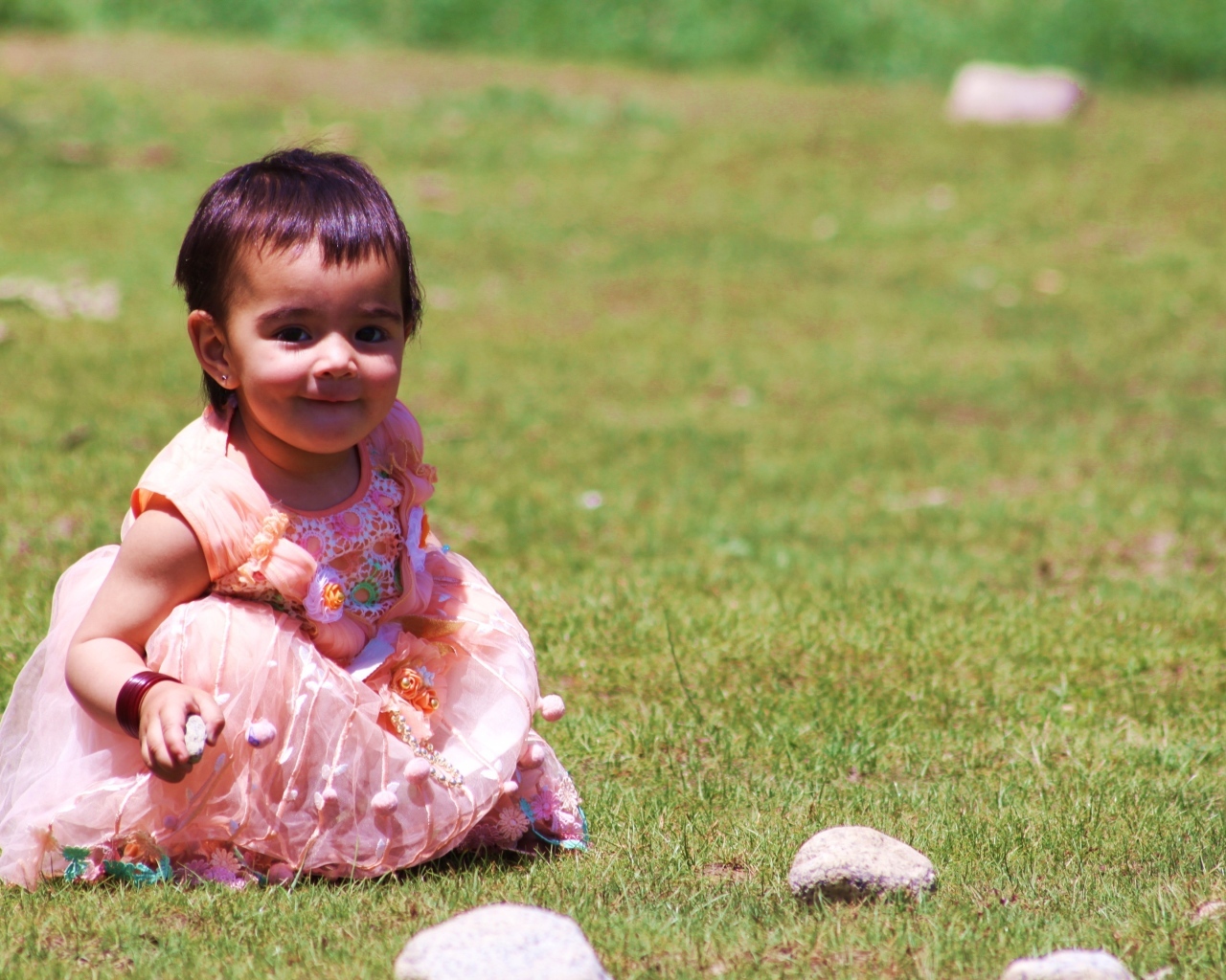 Девочка в розовом платье играет на зеленой траве