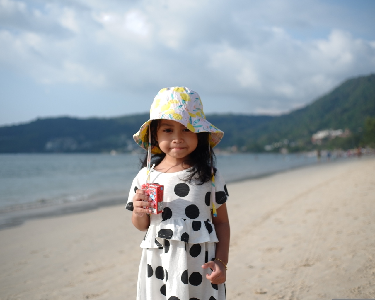 Девочка с соком в руках стоит на пляже