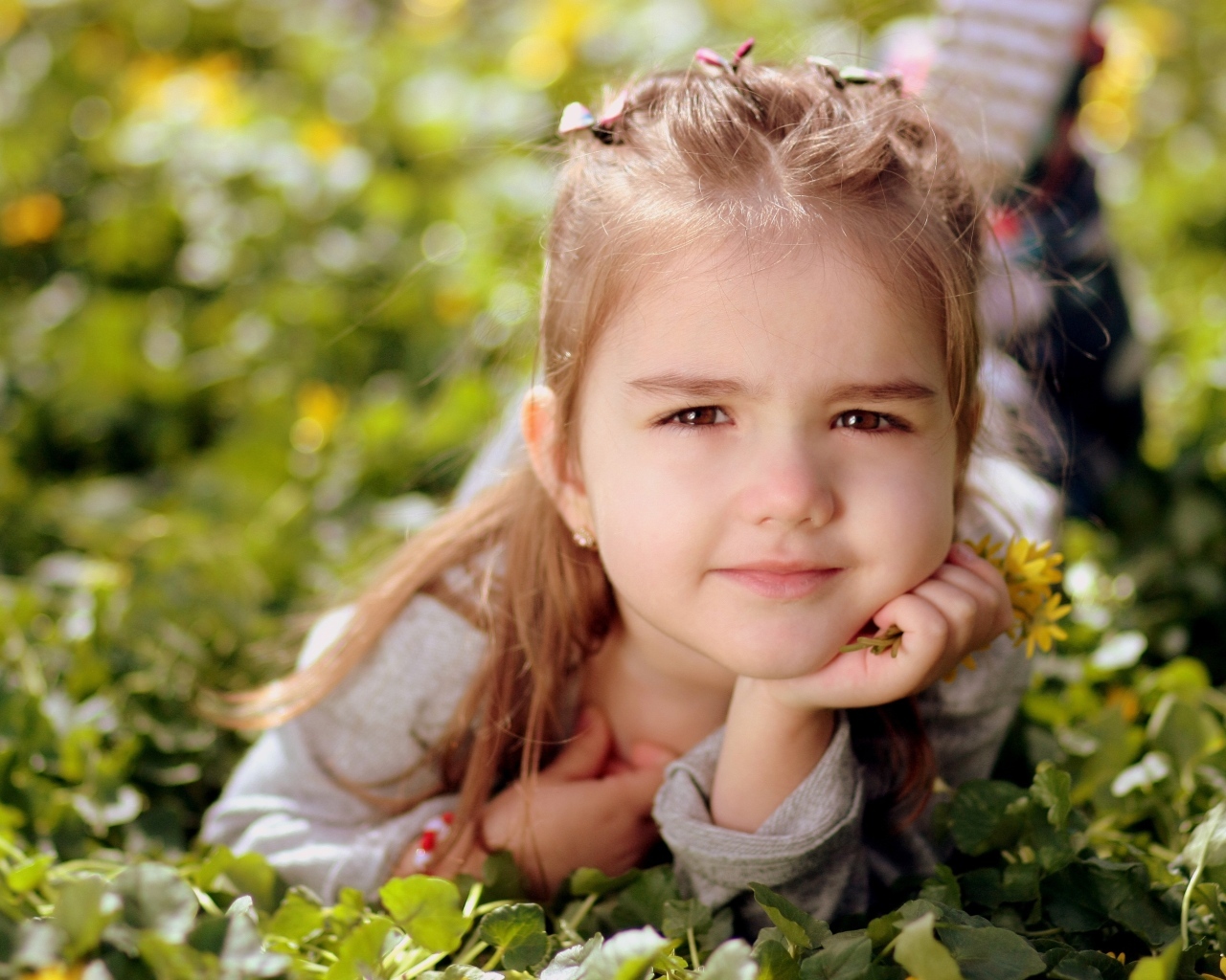 Маленькая кареглазая девочка лежит на траве с цветами