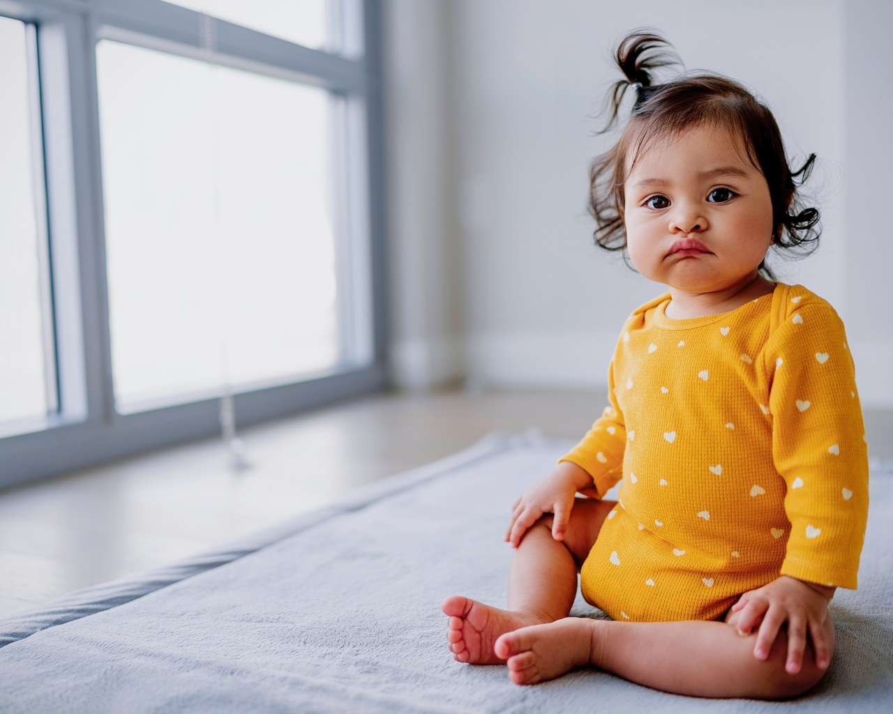 Маленькая смешная девочка сидит у окна