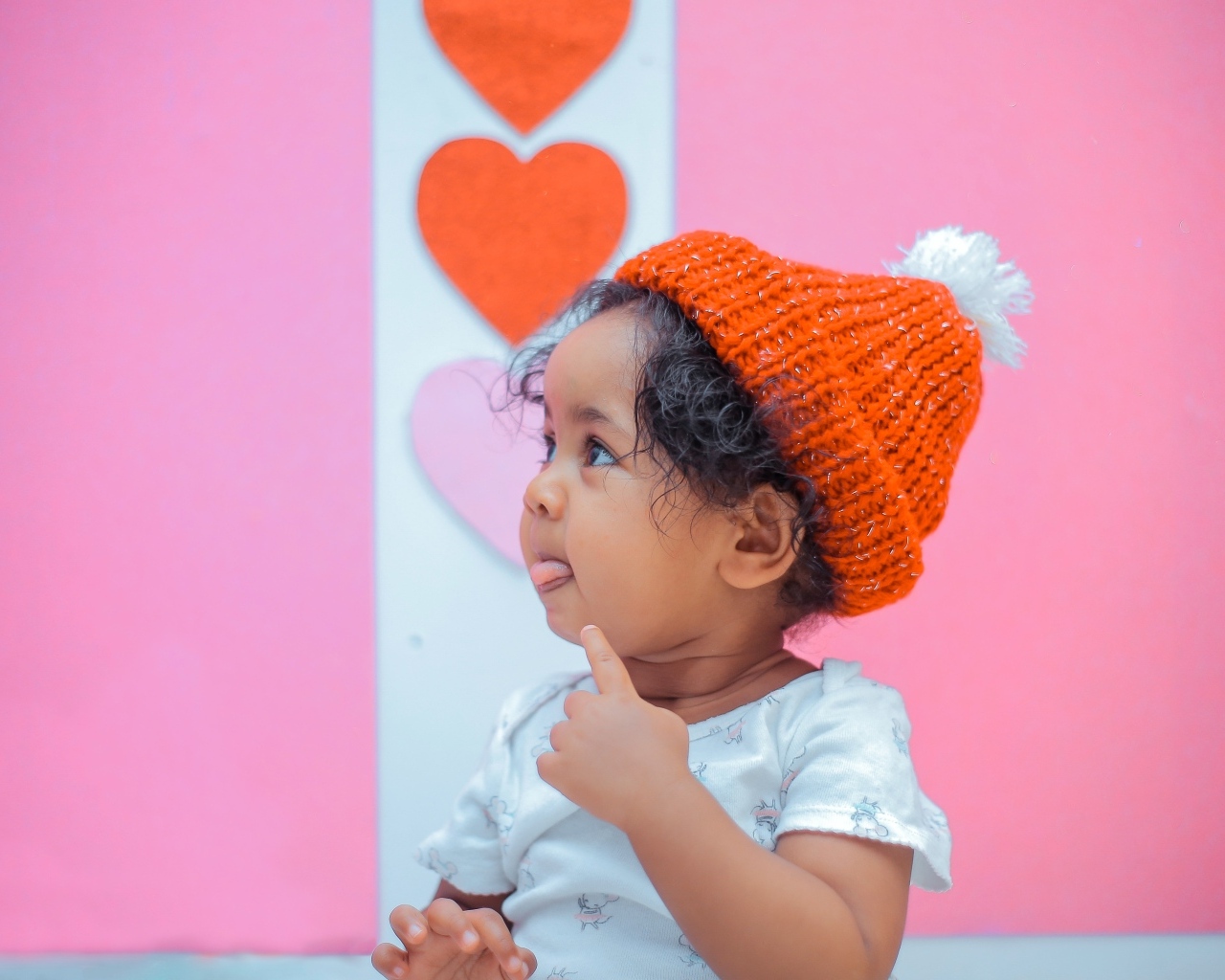 Маленькая девочка в вязаной шапке на розовом фоне