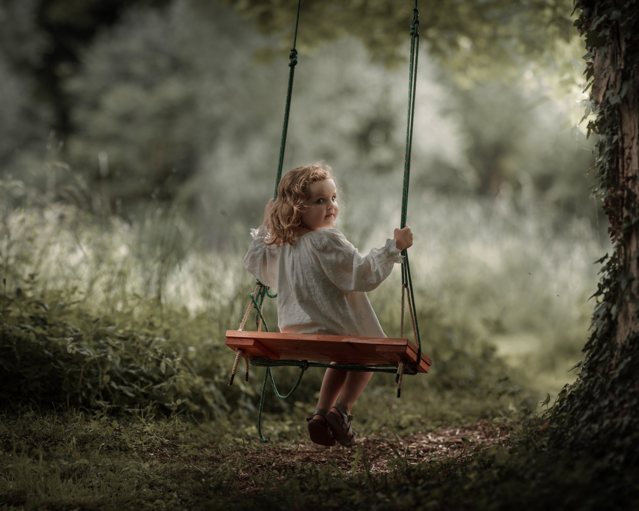 Маленькая девочка на качели в саду