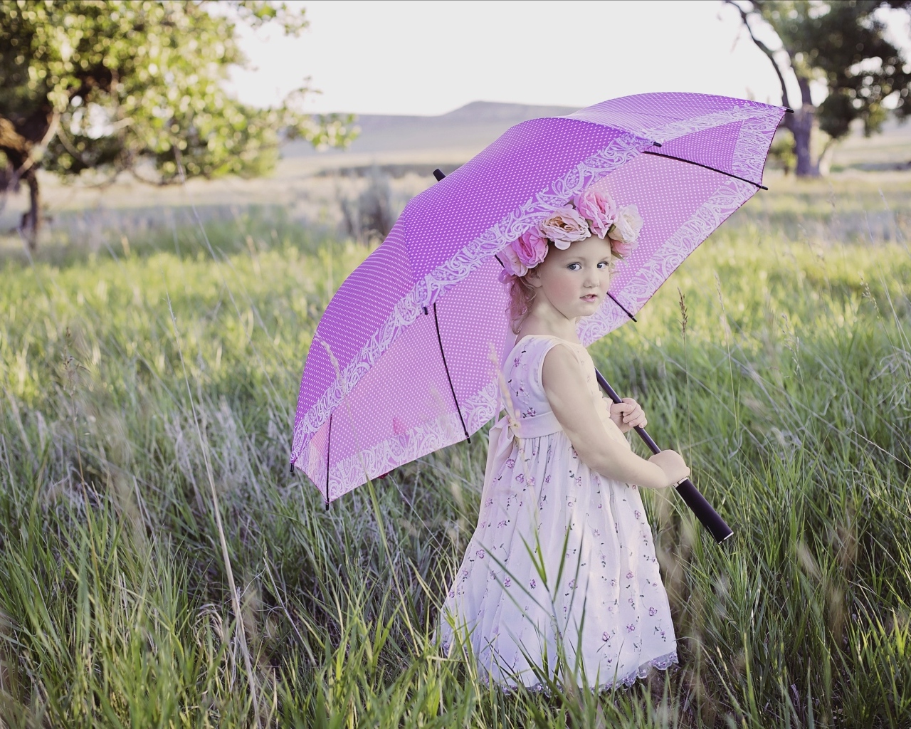 Маленькая девочка стоит в траве с зонтом