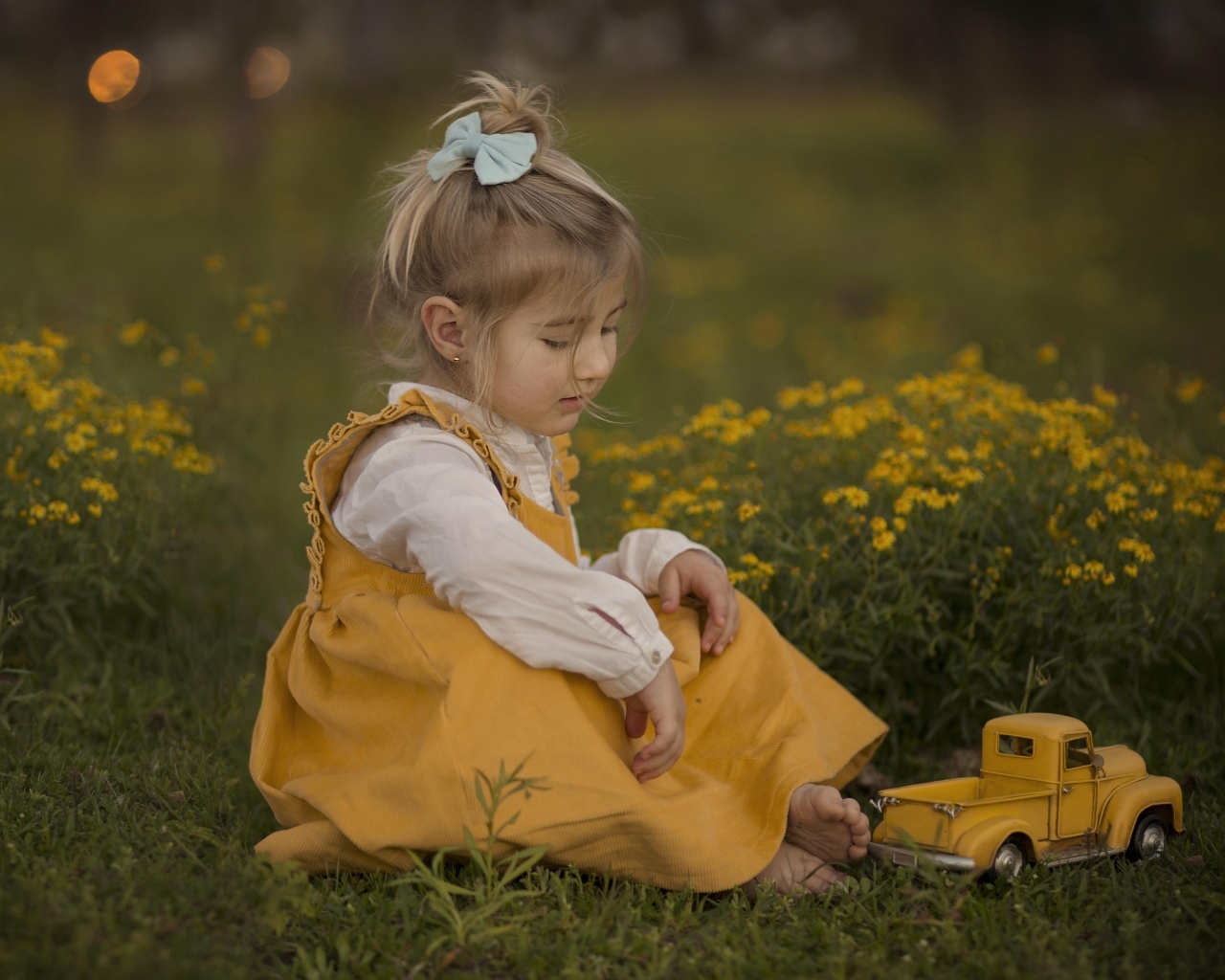 Маленькая девочка с игрушечной машиной сидит на траве