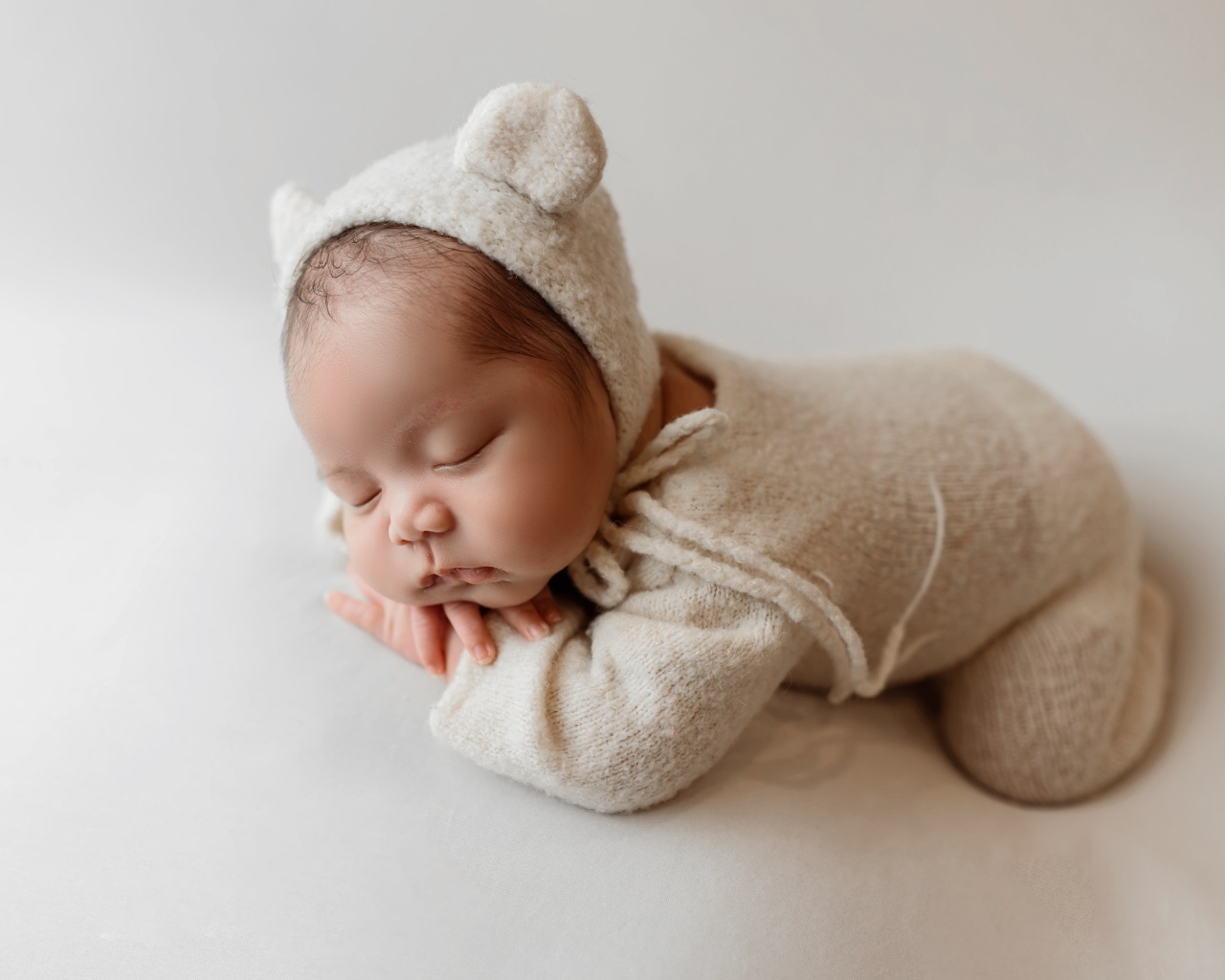 Маленький спящий ребенок в вязаном костюме на сером фоне