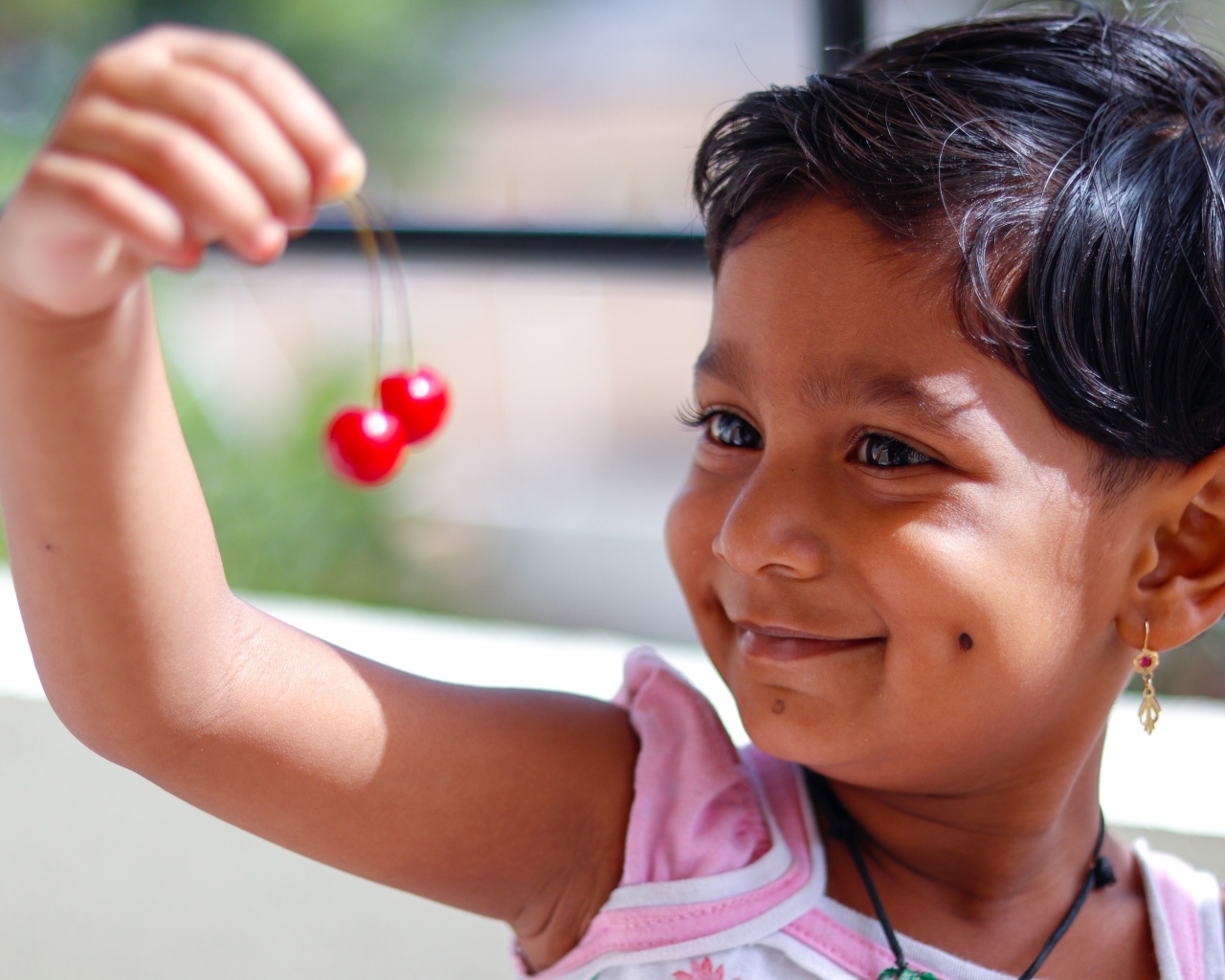 Маленькая улыбающаяся девочка с ягодами вишни в руках