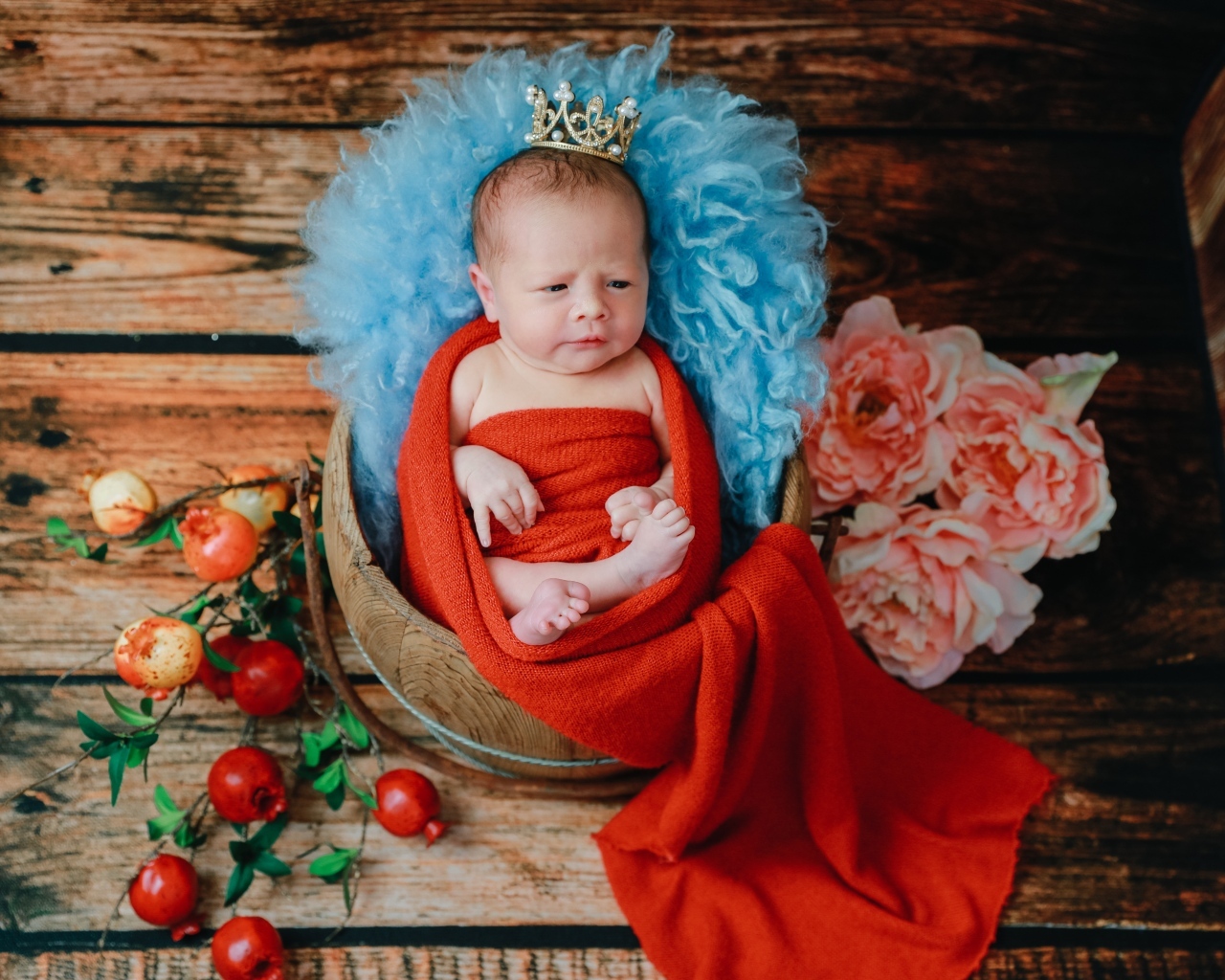 Новорожденный ребенок в красном покрывале с короной на голове 